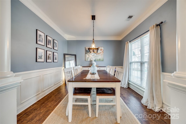 dining space featuring visible vents, wainscoting, dark wood-style floors, crown molding, and ornate columns