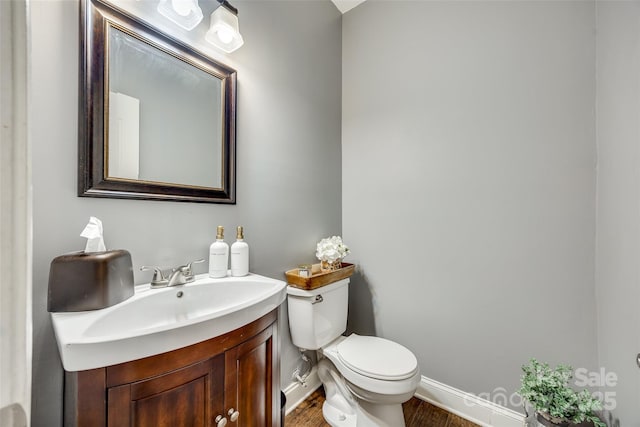 half bathroom featuring toilet, baseboards, and vanity