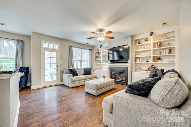 living room featuring baseboards, a glass covered fireplace, wood finished floors, and a healthy amount of sunlight