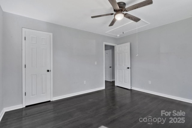 unfurnished room featuring attic access, dark wood-style flooring, and baseboards