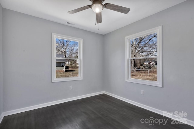 empty room featuring dark wood-type flooring, a wealth of natural light, visible vents, and baseboards