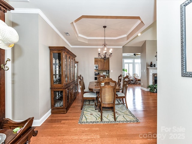 dining space featuring a tray ceiling, crown molding, a fireplace, visible vents, and light wood-style floors