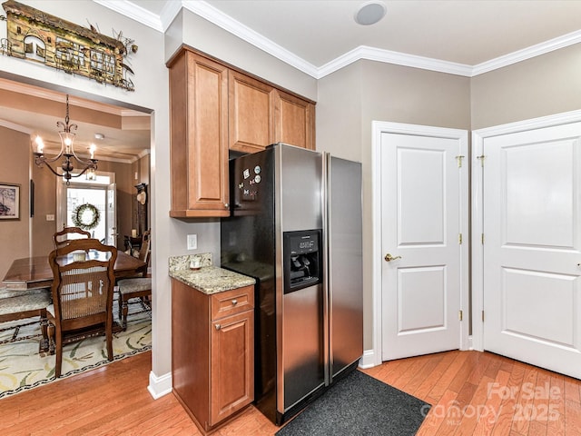 kitchen with light wood finished floors, stainless steel fridge, ornamental molding, brown cabinets, and light stone countertops