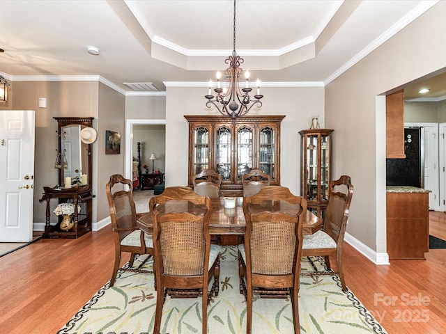 dining area featuring light wood finished floors, baseboards, a raised ceiling, and a notable chandelier