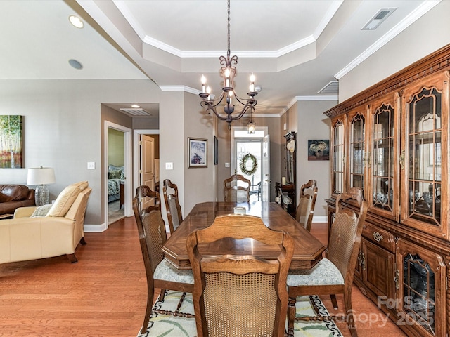 dining room featuring crown molding, a raised ceiling, visible vents, an inviting chandelier, and light wood-type flooring