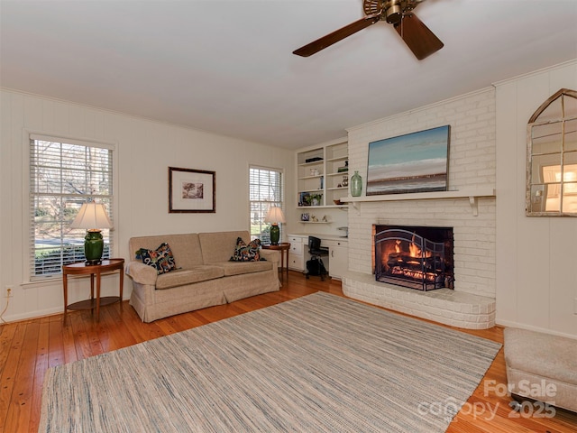 living area featuring hardwood / wood-style flooring, ceiling fan, a brick fireplace, and built in features