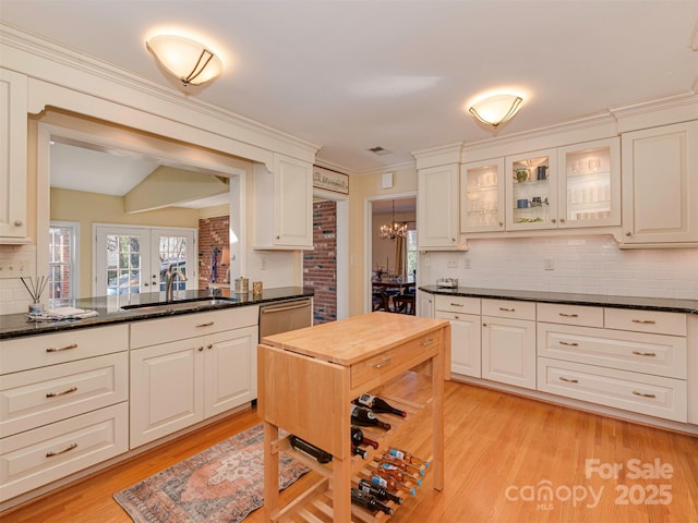 kitchen with stainless steel dishwasher, light wood-style flooring, a sink, and glass insert cabinets