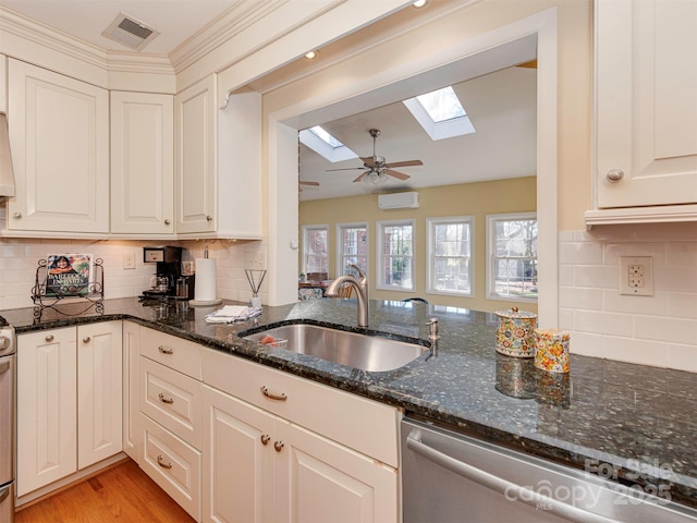 kitchen featuring dark stone counters, a skylight, a sink, and visible vents