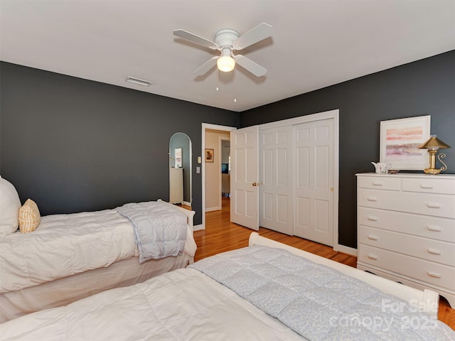 bedroom with visible vents, arched walkways, ceiling fan, light wood-style floors, and a closet