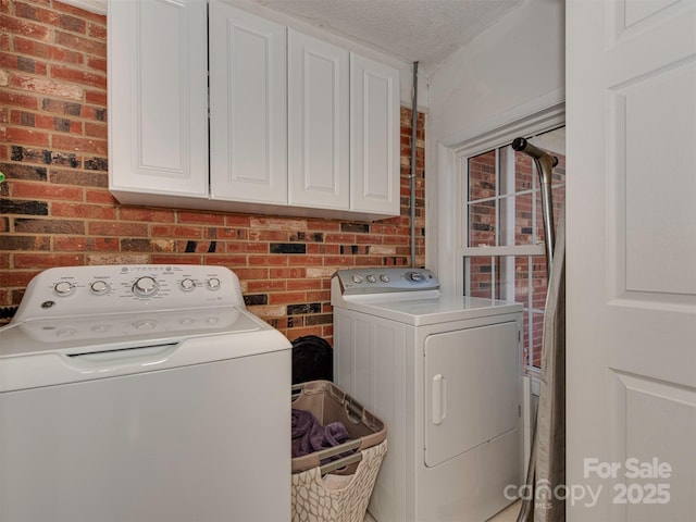 washroom featuring brick wall, cabinet space, a textured ceiling, and washing machine and clothes dryer