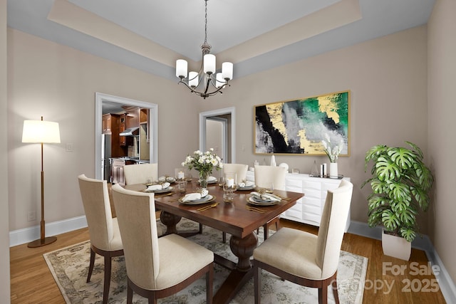 dining area with a chandelier, baseboards, a raised ceiling, and light wood-style floors