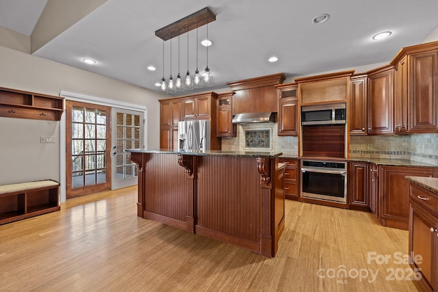 kitchen with a breakfast bar area, under cabinet range hood, stainless steel appliances, light wood-style floors, and french doors