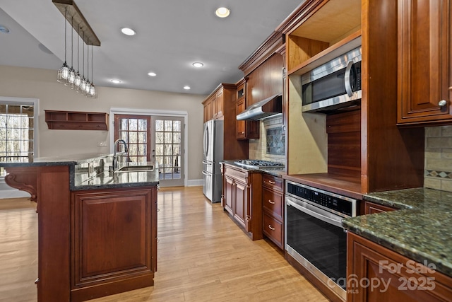 kitchen featuring plenty of natural light, an island with sink, wall chimney exhaust hood, appliances with stainless steel finishes, and a sink