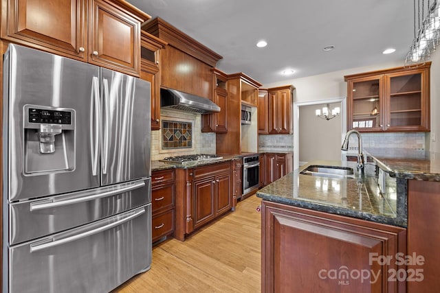 kitchen with stainless steel appliances, a sink, exhaust hood, light wood-type flooring, and glass insert cabinets