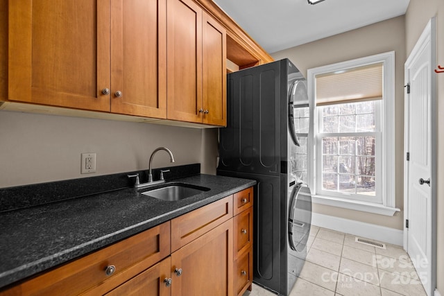 clothes washing area featuring light tile patterned floors, cabinet space, visible vents, a sink, and stacked washing maching and dryer