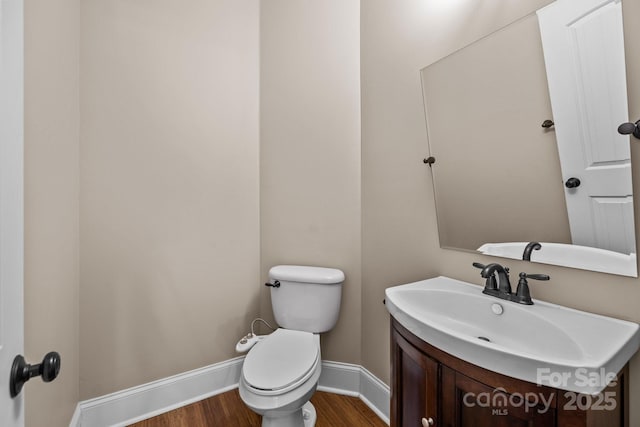 half bathroom with toilet, wood finished floors, vanity, and baseboards