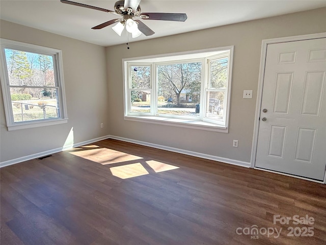 interior space with a ceiling fan, visible vents, dark wood finished floors, and baseboards