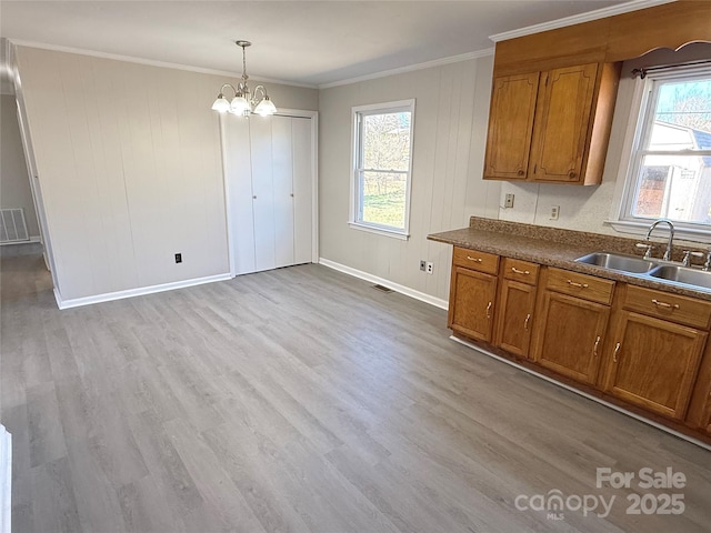 kitchen featuring light wood-style flooring, a sink, visible vents, brown cabinetry, and dark countertops