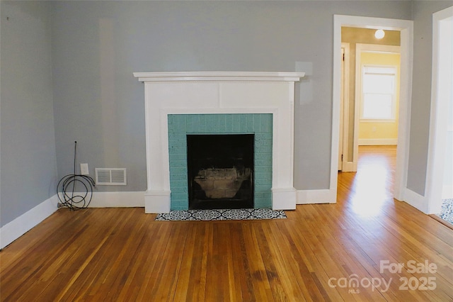 interior details featuring a brick fireplace, visible vents, baseboards, and wood finished floors