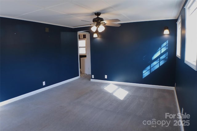 carpeted spare room featuring ceiling fan, baseboards, and crown molding