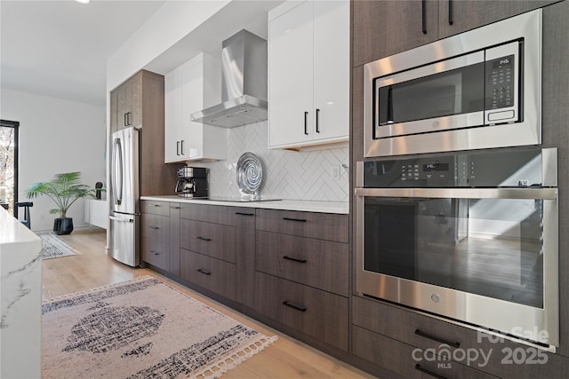 kitchen with tasteful backsplash, wall chimney exhaust hood, appliances with stainless steel finishes, light countertops, and white cabinetry