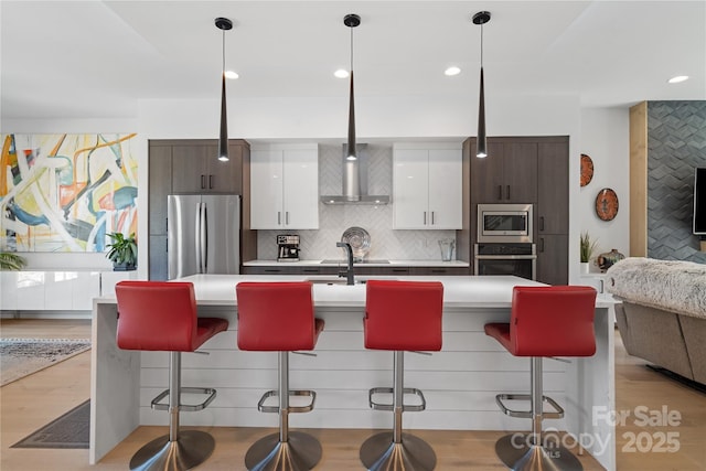 kitchen featuring stainless steel appliances, a breakfast bar, light countertops, backsplash, and light wood finished floors