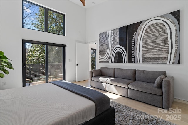 bedroom featuring access to outside, a towering ceiling, and wood finished floors