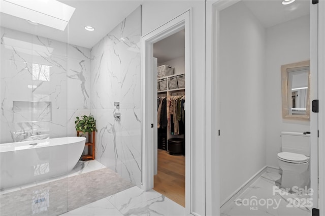 bathroom with stone wall, recessed lighting, a skylight, a freestanding bath, and marble finish floor