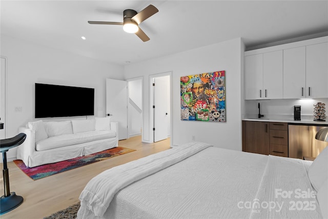 bedroom with light wood-style floors, indoor wet bar, and a ceiling fan