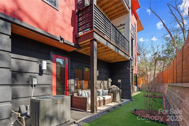 view of side of property featuring outdoor lounge area, a lawn, central AC unit, fence, and a balcony