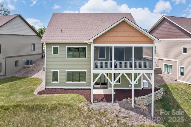 back of property with roof with shingles, a patio, central air condition unit, a lawn, and a sunroom