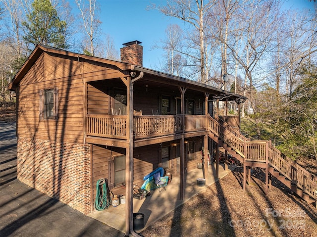 rear view of property featuring stairs, brick siding, a chimney, and a wooden deck