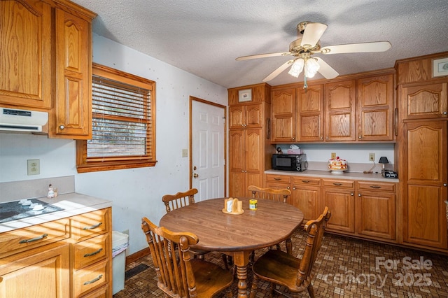 kitchen featuring brown cabinetry, white stovetop, light countertops, black microwave, and exhaust hood