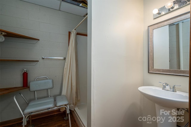 bathroom with a stall shower, concrete block wall, and wood finished floors