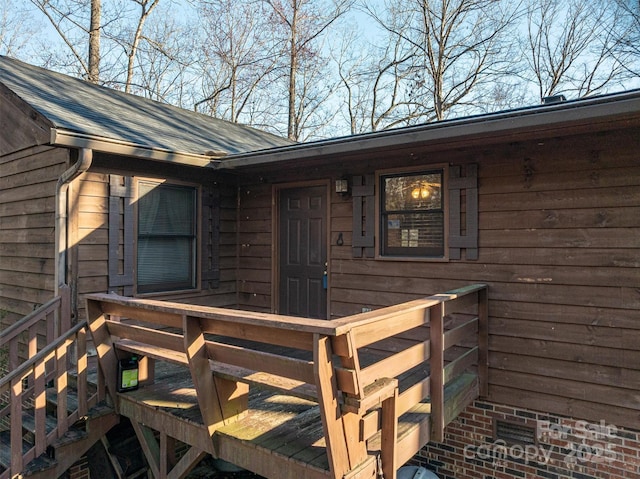 entrance to property featuring a shingled roof and a wooden deck