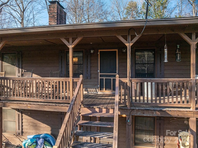 view of exterior entry with a porch, a chimney, and a balcony