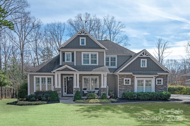 craftsman house featuring a shingled roof, covered porch, board and batten siding, a front yard, and stone siding