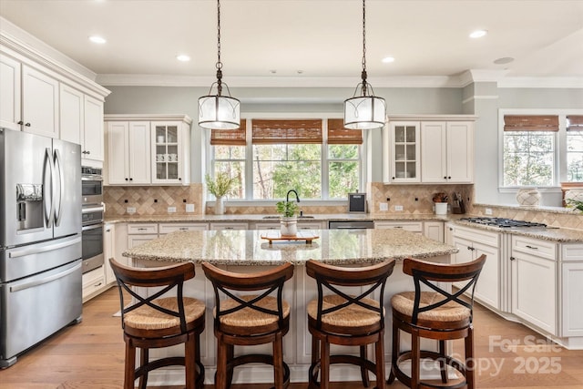 kitchen with appliances with stainless steel finishes, glass insert cabinets, a kitchen island, and white cabinetry