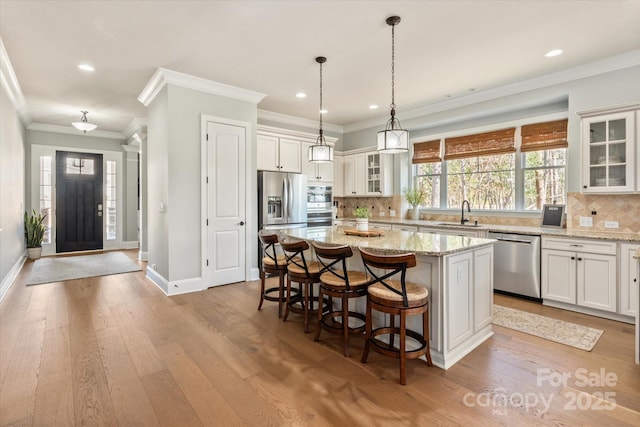 kitchen featuring a kitchen island, glass insert cabinets, hanging light fixtures, light stone countertops, and stainless steel appliances