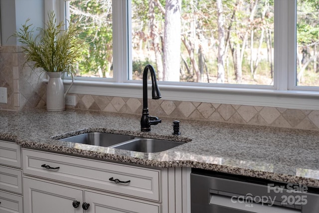 kitchen with light stone countertops, dishwasher, white cabinetry, and a sink