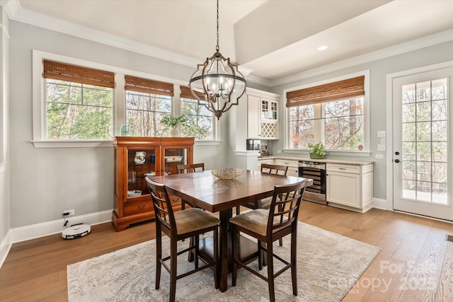 dining room with light wood-style floors, wine cooler, a wealth of natural light, and ornamental molding