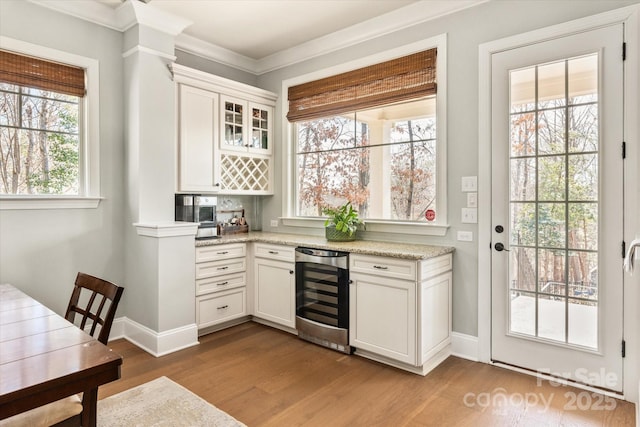 interior space with beverage cooler, baseboards, ornamental molding, a bar, and light wood-style floors