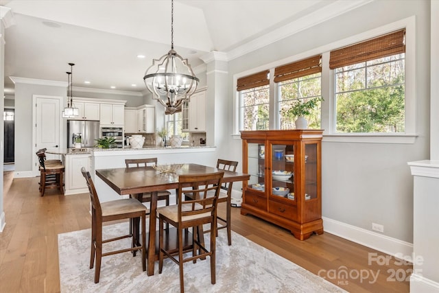 dining room featuring crown molding, baseboards, vaulted ceiling, and light wood finished floors