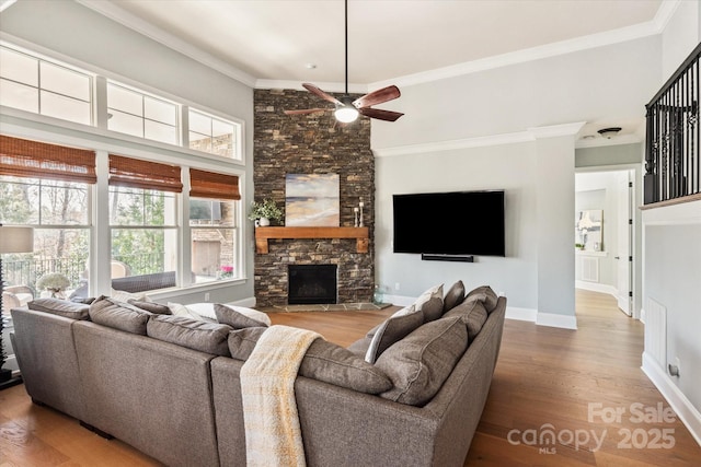 living area with baseboards, ceiling fan, wood finished floors, crown molding, and a stone fireplace