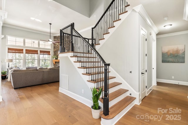 stairs featuring crown molding, a towering ceiling, a ceiling fan, wood finished floors, and baseboards