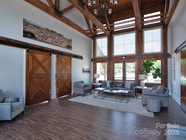 living area with a barn door, a high ceiling, dark wood finished floors, and beam ceiling