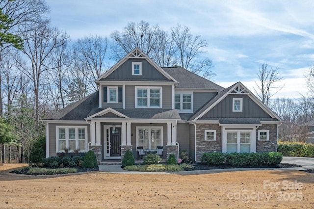 craftsman-style house featuring stone siding, covered porch, roof with shingles, and board and batten siding