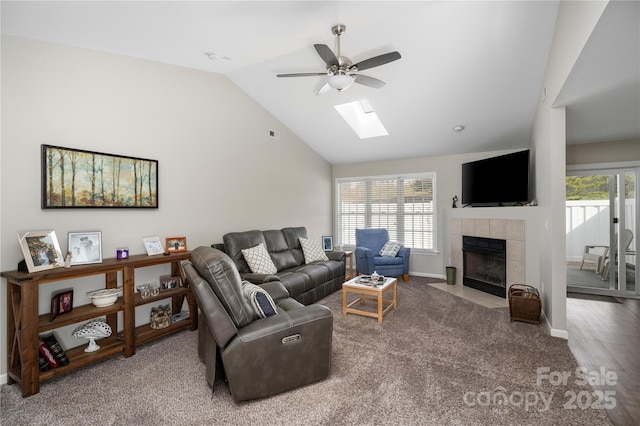 living room with visible vents, baseboards, a tiled fireplace, lofted ceiling with skylight, and ceiling fan