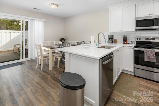 kitchen with stainless steel appliances, light countertops, white cabinetry, a sink, and a peninsula