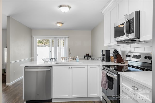 kitchen with stainless steel appliances, tasteful backsplash, white cabinetry, a sink, and a peninsula